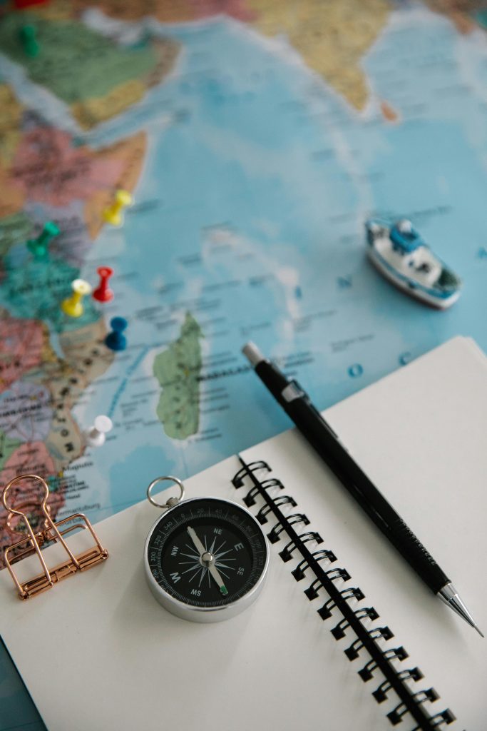 pexels-photo-8828668-8828668 Flat lay of travel essentials including a navigational compass, pencil, notepad, and map for trip planning.